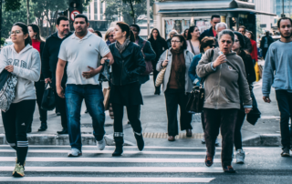 People crossing a city street, representing everyday participation in the economy and community life.